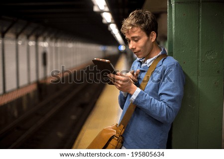 Young caucasian man in New York City subway station platform using tablet pc computer