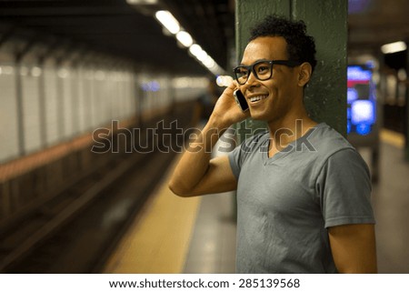 Young African Asian man in New York City in subway station talking on cell phone