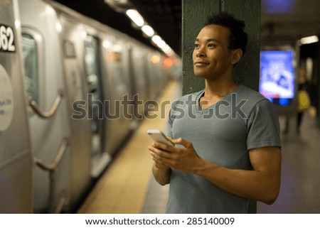 Young African Asian man in New York City in subway station texting cell phone