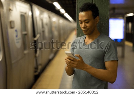 Young African Asian man in New York City in subway station texting cell phone