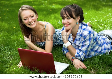 Two attractive girls on the grass with a laptop in the park