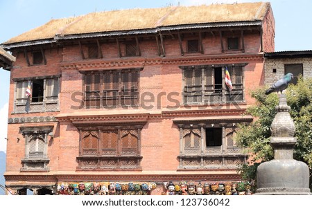 Red brick and thatch roof building with carved wooden windows and tibetan flags, hindu and buddhist  masks on the grooundfloor, Swayambhunath Stupa area, Kathmandu, Nepal.