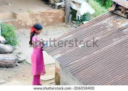 DHAMPUS, NEPAL - OCTOBER 8: Small nepalese young woman cuts onions-pot over  tin roof of shed-courtyard on October 8, 2012 in Dhampus village-Annapurnas Tour trekking route-foothills of the Himalayas.