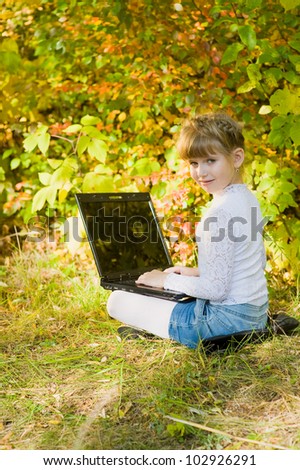 Little girl sitting on grass with laptop in the park