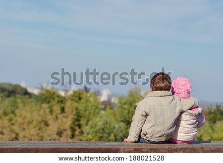 Little brother and sister are sitting on a bench above a precipice