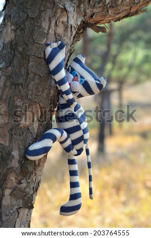 Striped handmade toy cat hanging on a tree