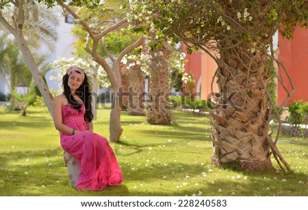 Pretty brunette in pink dress resting in hotel garden