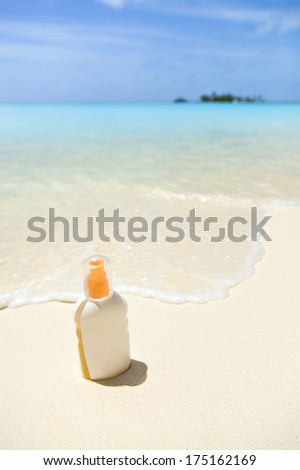 a tube of sunblock on the sandy beach, against the turquoise sea
