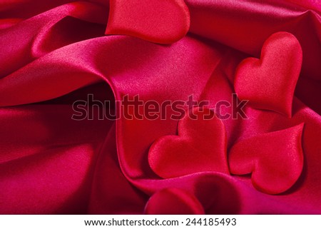red heart Valentine\'s Day symbols on red silk background close up