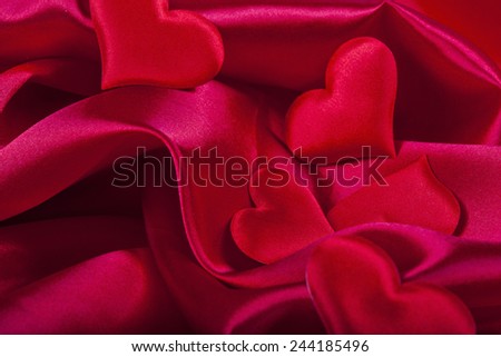 red heart Valentine\'s Day symbols on red silk background close up