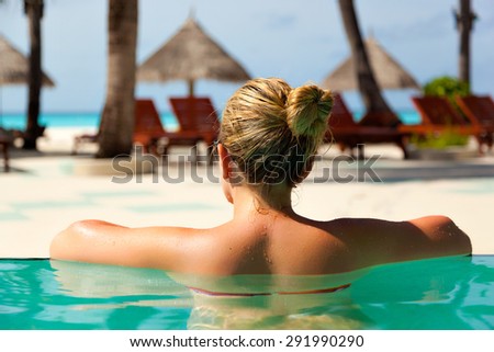 young woman in the pool looking back at the turquoise Caribbean sea on Bahamian beaches of the Maldives