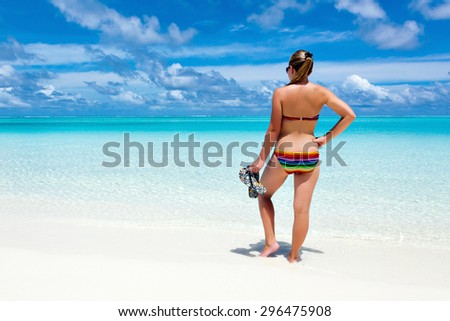 Young girl woman\'s back on the beach Caribbean turquoise sea on Maldivian Hawaii with slippers in hands