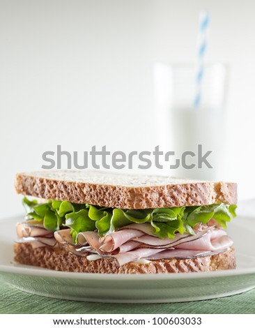 deli meat sandwich with ham, lettuce and mayo with glass of milk in background and copy space