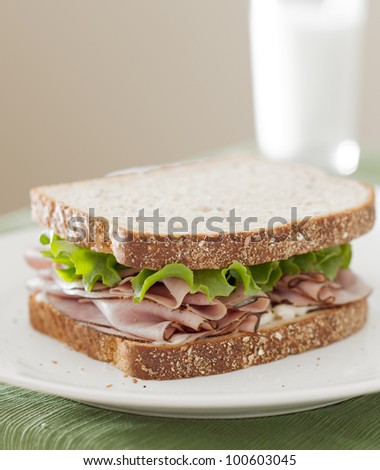 deli meat sandwich with ham, lettuce and mayo with glass of milk