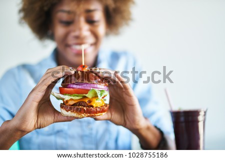 smiling african woman about to eat a meatless vegan cheese burger