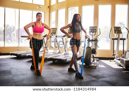 two woman working out in gym using resistance bands