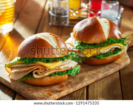 two cold cut style turkey and cheese sandwiches on pretzel buns