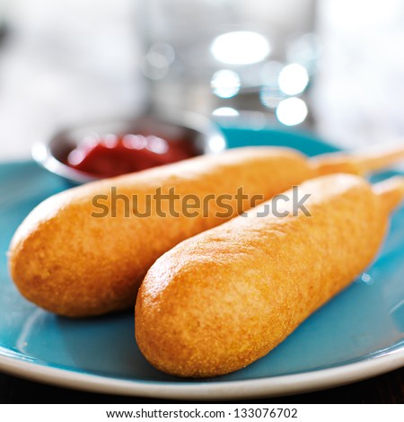 two corn dogs on a plate with ketchup close up