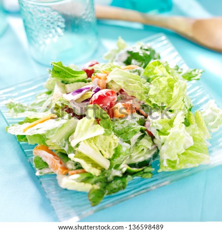 garden salad with fresh vegetables and ranch dressing on glass plate.