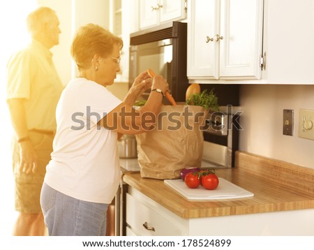 Elderly couple putting away groceries at home
