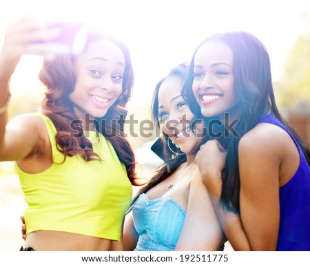 three african girls taking selfies with smart phone with lens flare in background.
