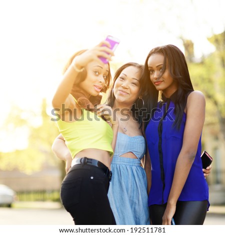 group of three girls wearing bright clothes taking selfies with smart phone