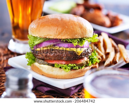 hamburger with fries and beer shot in panorama style with chicken wings in background