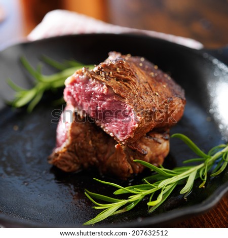 rare steak cut in half on iron skillet with rosemary