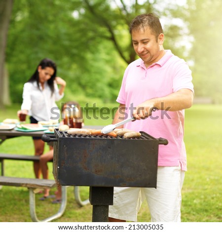 family barbecue - dad grilling with wife and daughter