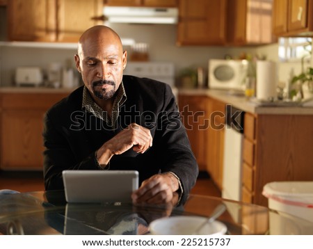 mature african man in kitchen using tablet