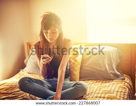 tech savvy asian teen girl using smart phone in bed room