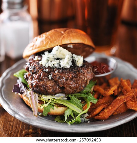 gourmet burger with blue cheese and sweet potato fries on metal plate.