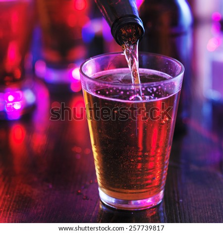 filling glass with beer from the bottle in colorful bar, lighting is super colorful to represent lighting you would see in a club or pub.