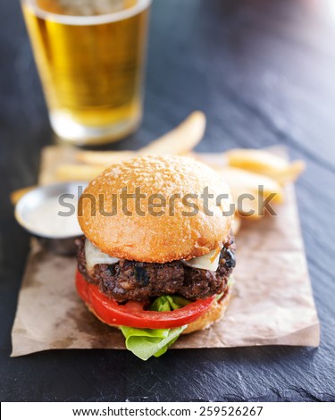 burger beer and fries served with sauce on slate surface atop wax paper