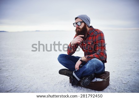 beard lumbersexual hipster sitting on suitcase in deep thought