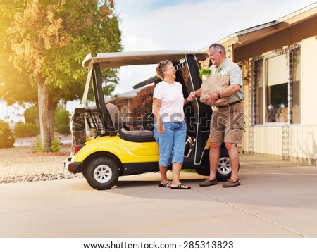 active senior couple coming home with groceries on golf cart