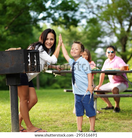 mother and son high fiver beside barbecue grill at picnic