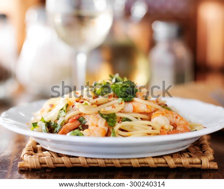 eye level view of shrimp spaghetti pasta on a white plate and white wine in background