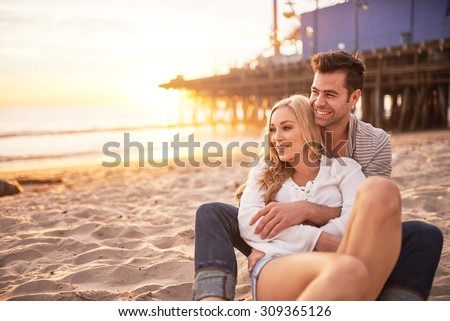 two lovers sitting on sand at santa monica beach during sunset