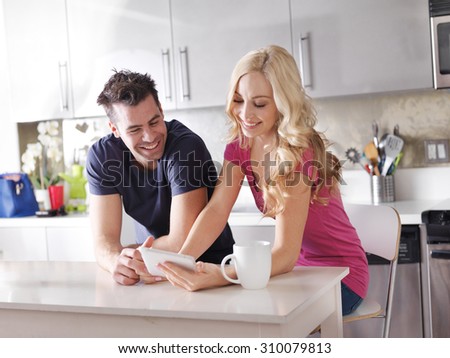 happy couple using tablet pc to shop online or watch videos in kitchen at breakfast
