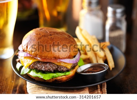 cheeseburger and fries on plate served with beer at restaurant