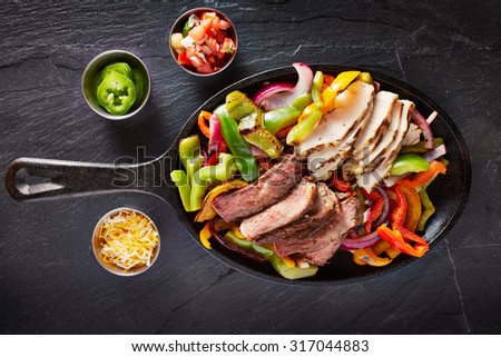 aerial view of a iron skillet filled with steak and chicken mexican fajitas on slate