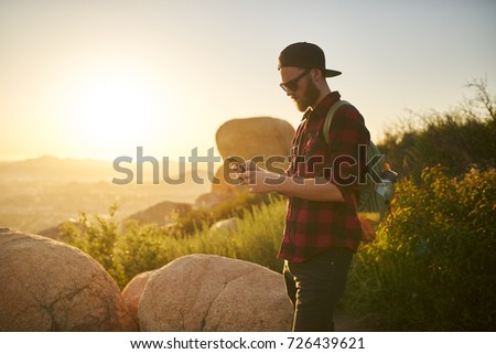 bearded millennial hiker using smartphone during hike