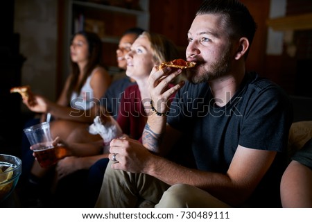 man eating pizza while watching tv at night with friends