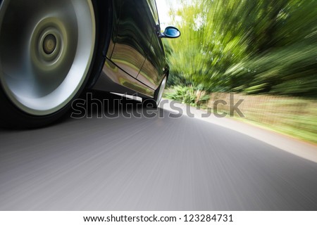 Rear side view of black family car driving fast on forest road