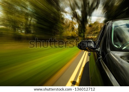 Side view of black car driving in the forest with heavy blurred motion.