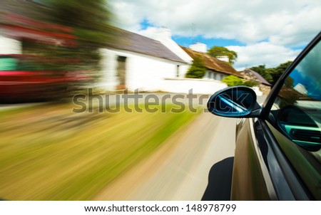 Mirror view of black car driving in village.