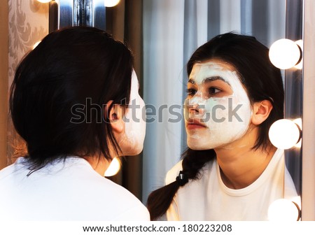 Asian woman looking in the mirror with mask on her face
