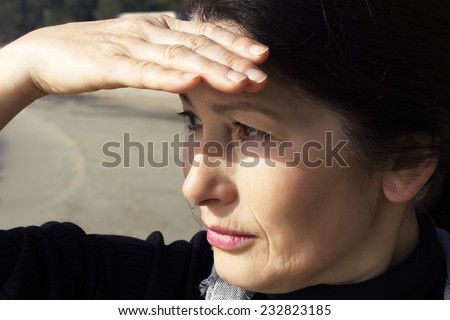 Portrait of beautiful Asian woman looking into the distance, holding  hand blocking her eyes from the sun.