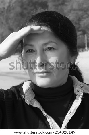 Portrait of beautiful Asian woman looking into the distance, holding hand blocking her eyes from the sun.